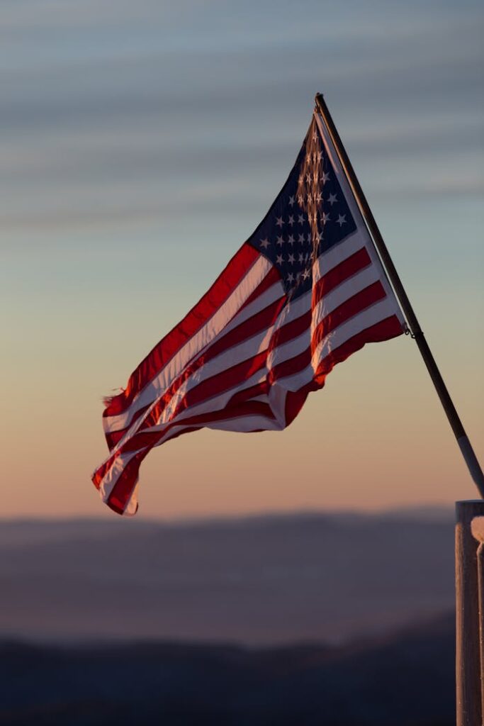 A vibrant US flag waves against a scenic sunset backdrop in Stowe, Vermont.